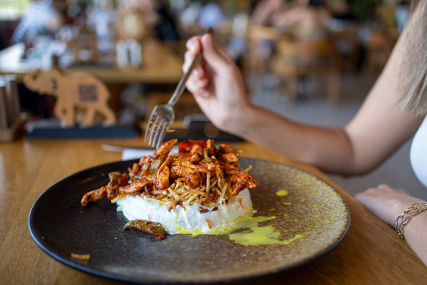 一个女人在餐馆里手里拿着叉子吃鸡肉。库存图片图片下载