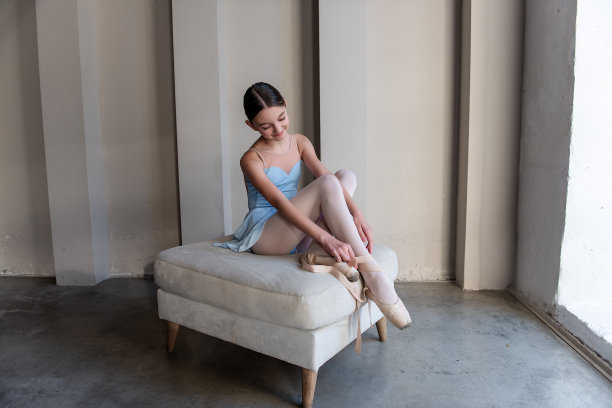 年轻安详的芭蕾舞女演员优雅地坐在奥斯曼上系着尖头鞋的带子图片下载
