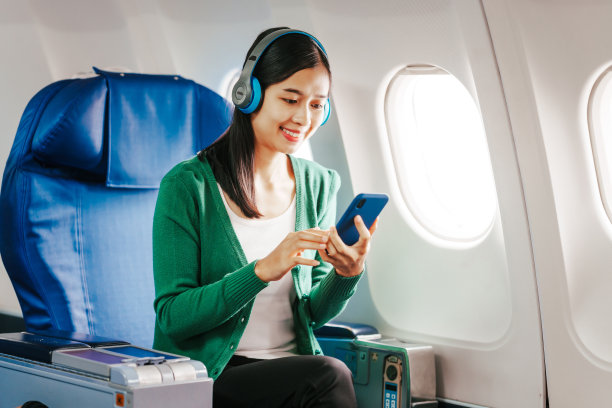 一个年轻的亚洲女人，一个飞机乘客，通过她的手机听音乐放松。她在长途旅行中使用科技来放松。图片下载