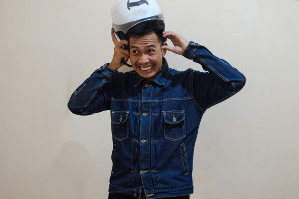 一名东南亚男子身穿牛仔夹克，头上戴着白色摩托车头盔图片下载