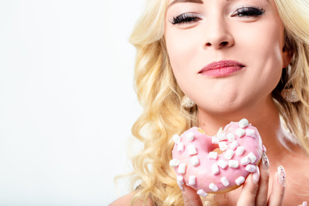 迷人的金发女人正在吃一个裹着棉花糖的粉色甜甜圈图片下载
