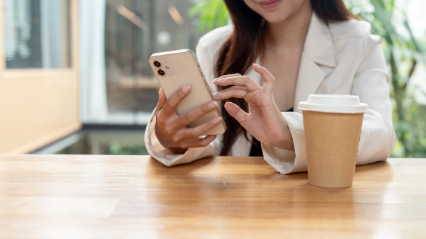 一张裁剪过的照片，一位美丽的亚洲女商人坐在咖啡店里，用她的智能手机。图片下载