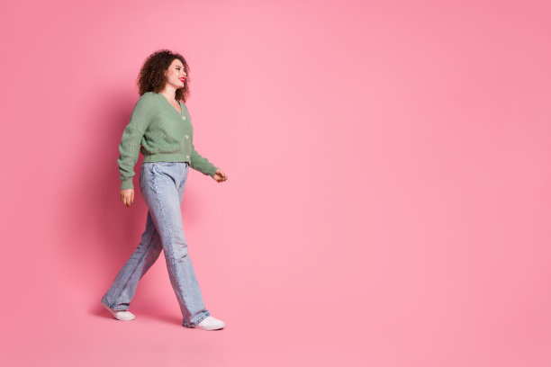 照片中，开朗可爱的女人穿着时髦的卡其色衣服，在粉红色的背景下孤独地走着图片下载