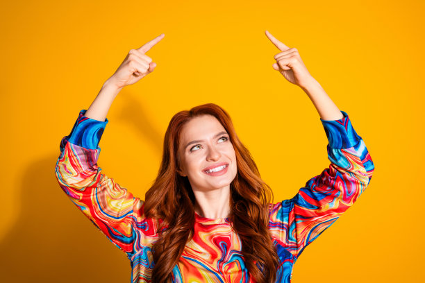 照片中迷人的年轻女子抬头看空，穿着时尚的彩色衣服，孤立在橙色的背景上图片下载