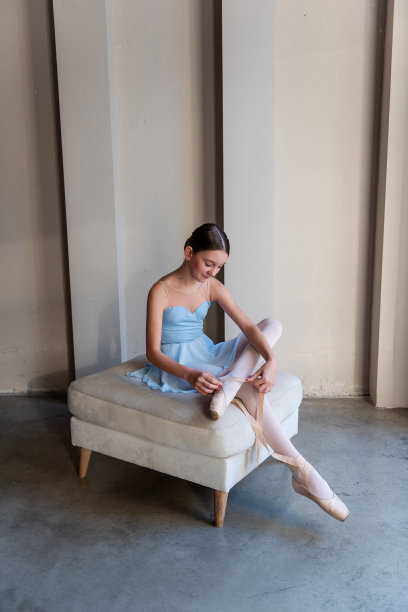年轻安详的芭蕾舞女演员优雅地坐在奥斯曼上系着尖头鞋的带子图片下载
