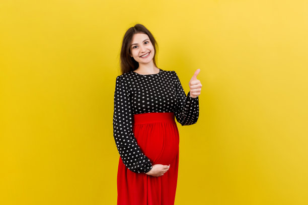 快乐的孕妇在彩色背景下对着肚子竖起大拇指。幸福的孕妇。本空间图片下载