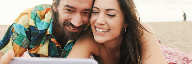 情侣们在沙滩上放松，用手机看视频和照片，全景图片下载