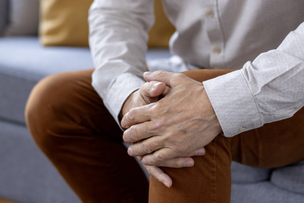 身体部分照片，老人的手握着棕色裤子的腿膝盖，感到剧烈的疼痛和扭伤图片下载