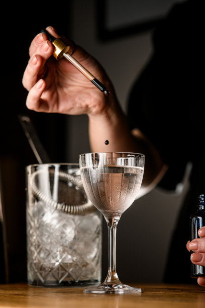 一位调酒师的女性双手将一滴棕色液体滴进透明的饮料中图片下载