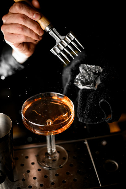 装有棕色饮料的玻璃杯，酒保的手在上面用冰锥敲碎冰块图片下载