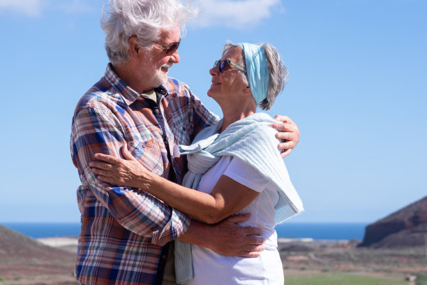 暑假里，山地户外活动的老夫妇愉快地拥抱在一起，享受健康的生活方式和自由。蔚蓝的天空和水面上的地平线图片下载