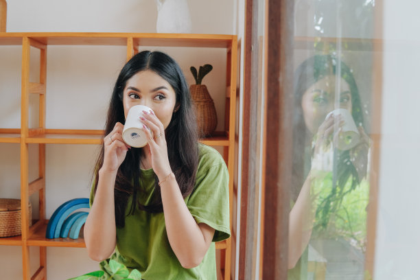 穿着绿色t恤的年轻亚洲女子正在喝水。图片下载