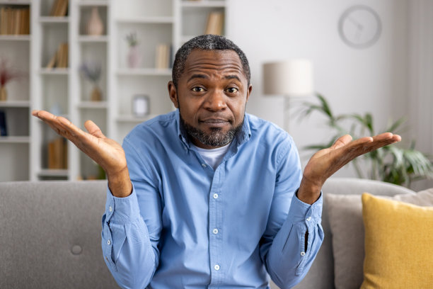 困惑的男人坐在家里的沙发上耸耸肩图片下载