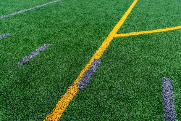 下午晚些时候的特写照片，在一个人造草坪上，灰色的足球hash标记和黄色的足球线。图片下载