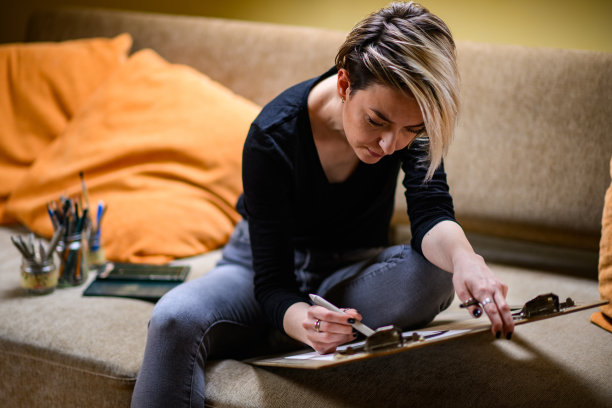 年轻有灵感的艺术家坐在家里的沙发上用铅笔画画。图片下载