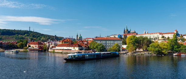 这是一张河的照片，背景是船和建筑物。秋天伏尔塔瓦码头上的游船。布拉格的景色。图片下载