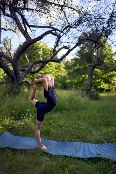 5岁的小女孩穿着黑色的极简主义服装，在室外的花园里做体操图片下载