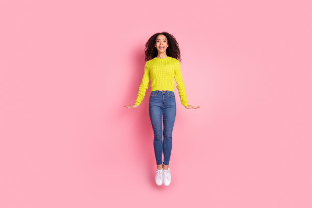 运动的青年有趣的女孩穿着绿色毛衣和牛仔裤跳蹦床的全身长度的照片孤立在粉红色的背景图片下载