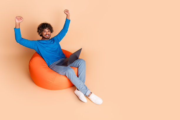 照片中快乐开朗的好人穿着时髦的蓝色衣服，坐在沙发上，在米色的背景上购买空的空间图片下载