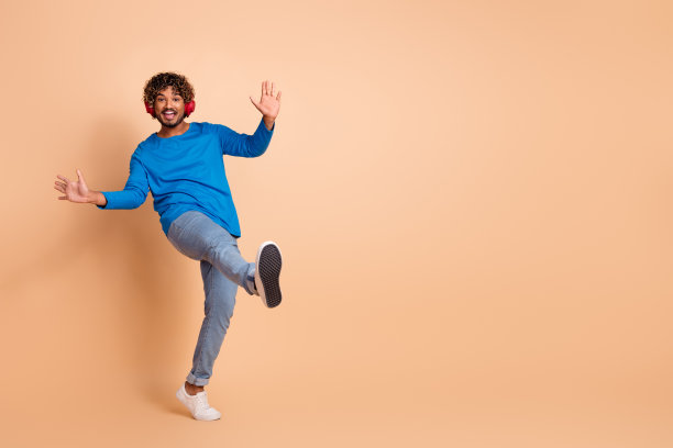 照片的快乐积极的男人穿着时髦的蓝色衣服听音乐播放列表的歌曲空的空间孤立在米色的背景图片下载