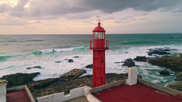 美丽的灯塔在黄昏时闪耀着岩石海岸。历史信标闪烁图片下载