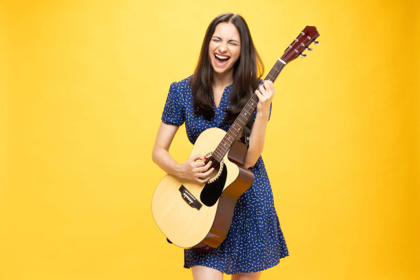 开朗可爱的女孩穿着时髦的衣服，拿着吉他乐器，在黄色背景照片上玩得很开心图片下载