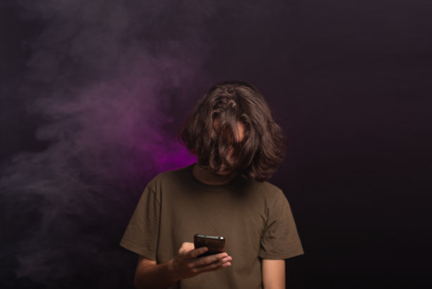 英俊的长发年轻人低头看手机的照片。图片下载