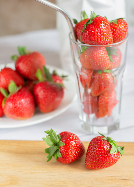 熟的，多汁的，红色的草莓在一个玻璃杯和盘子里放在厨房的桌子上，垂直照片图片下载