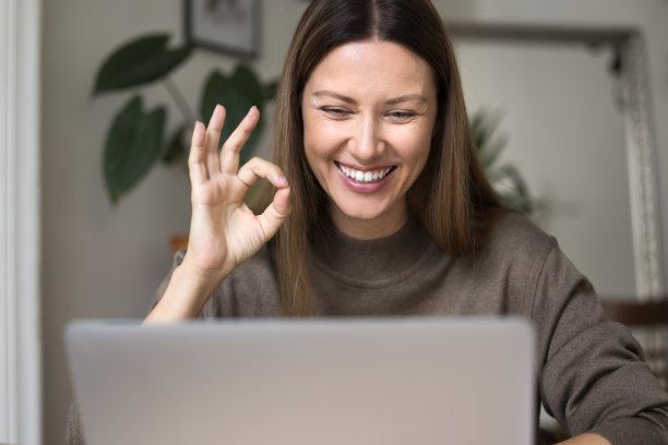 开朗的自由职业女性对着笔记本电脑做着OK的手势图片下载