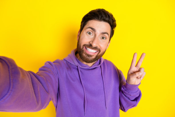 照片中，帅气的年轻人自拍，v字星座的人穿着时髦的紫色衣服，孤立在黄色的背景上图片下载