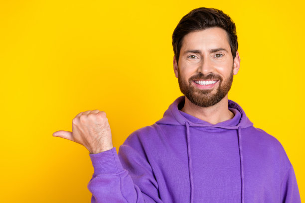 照片满意的男人与时尚的鬃毛穿着紫色卫衣指向折扣空间孤立的黄色背景图片下载