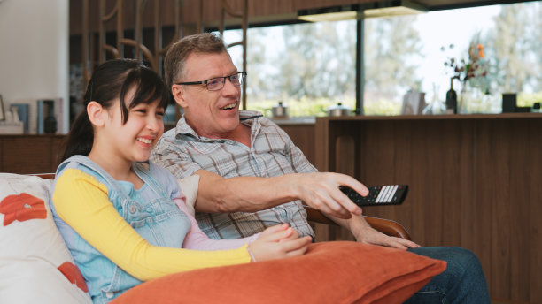 慈祥的爷爷和可爱的孙女一起看电视。散度。图片下载