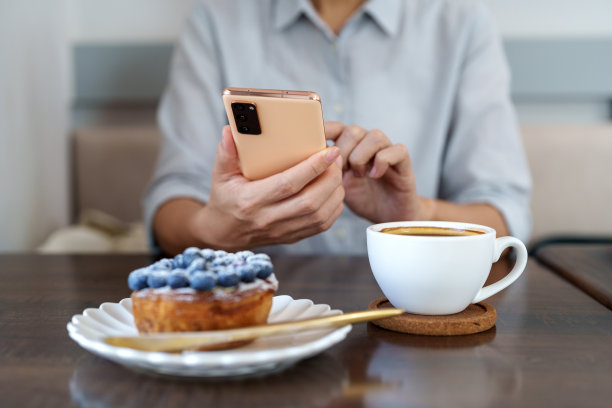 一名亚洲女性坐在咖啡馆里用智能手机享受咖啡休息的图片。图片下载