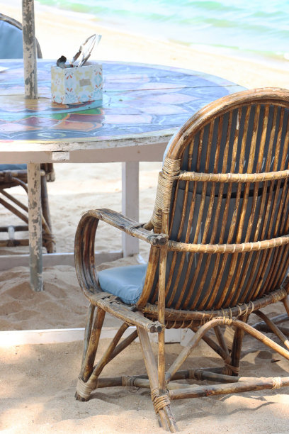 竹制扶手椅的特写图片，上面有圆形的桌子，面朝日落时的大海，海滩餐厅的露天用餐区俯瞰大海，戏剧性的橙色天空背景，后视图，重点放在前景上图片下载