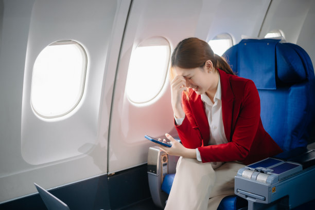 一位沮丧的女士坐在飞机上，双手抱头的照片。一位亚洲女士坐在座位上图片下载