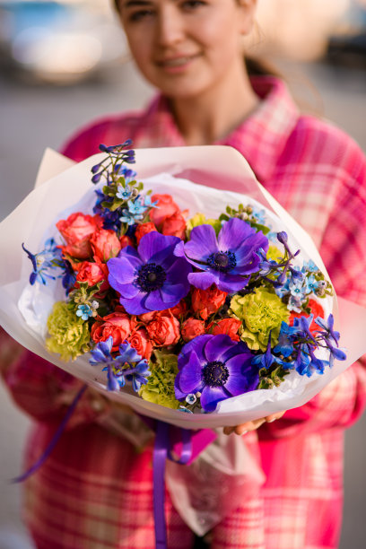 美丽的女人面带微笑，手里拿着一束用包装纸包裹着的五颜六色的花图片下载