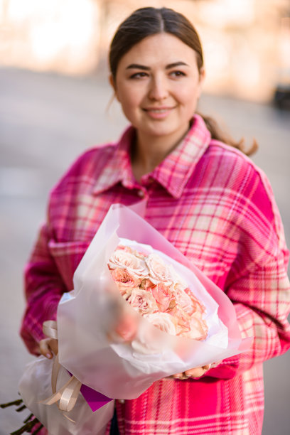 微笑的女孩在粉红色拿着一束美丽的玫瑰包装在模糊的背景图片下载