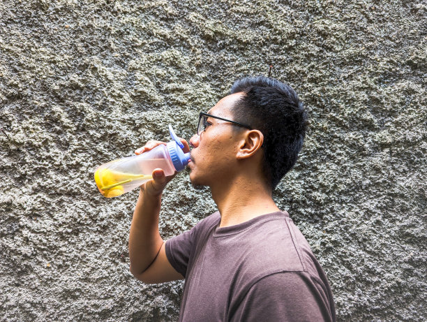 一名东南亚男子喝着注入水柠檬和草柠檬，装在瓶子里，放在户外图片下载