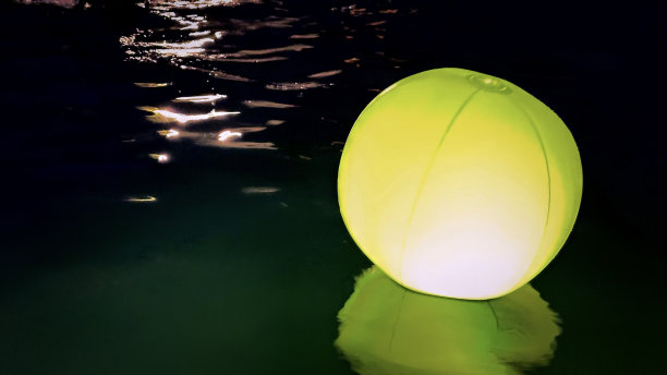 反射发光霓虹黄色沙滩球漂浮在游泳池在夜晚夏天背景复制空间•股票照片图片下载