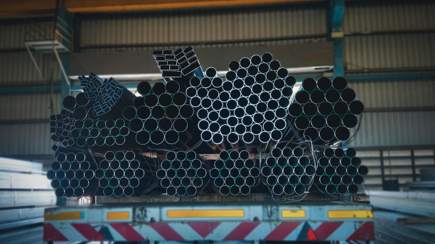 堆叠的钢管与建筑钢材，黑色管道，金属管，特写单色照片与选择性聚焦，堆叠的许多管道在建筑工地图片下载