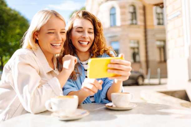 两个年轻女子，姐妹，最好的朋友，在智能手机上展示新闻社交媒体照片，坐在咖啡馆里喝咖啡，吃早餐。图片下载