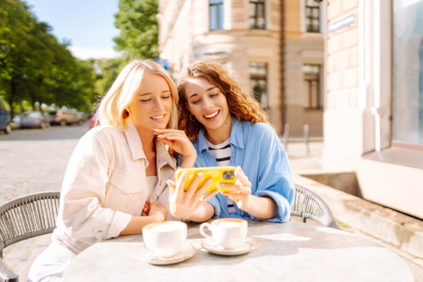 两个年轻女子，姐妹，最好的朋友，在智能手机上展示新闻社交媒体照片，坐在咖啡馆里喝咖啡，吃早餐。图片下载