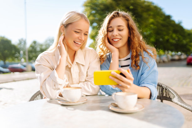 两个年轻女子，姐妹，最好的朋友，在智能手机上展示新闻社交媒体照片，坐在咖啡馆里喝咖啡，吃早餐。图片下载