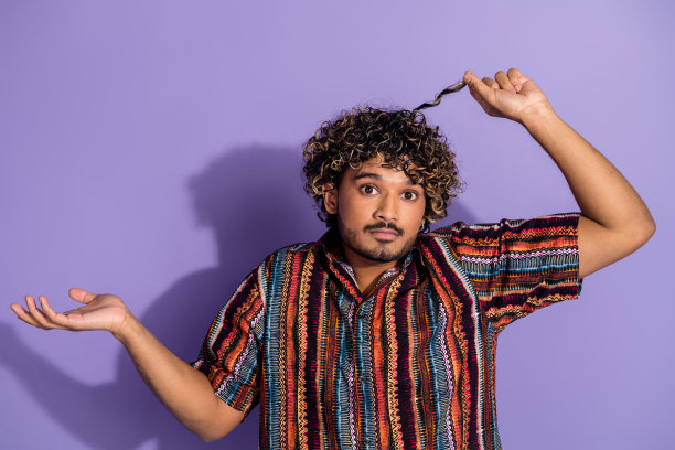 照片上的男人满脸胡须，卷发，穿着印花衬衫，手臂挽着卷发，孤立在紫色的背景上图片下载