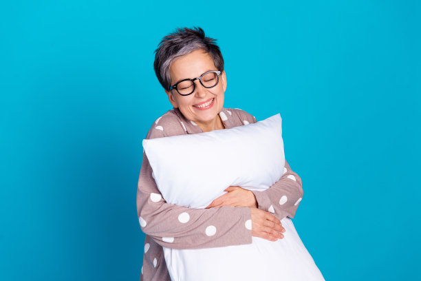 好心情的照片漂亮可爱的高级妇女穿着时髦的睡衣抱柔软的枕头孤立在蓝色的背景图片下载