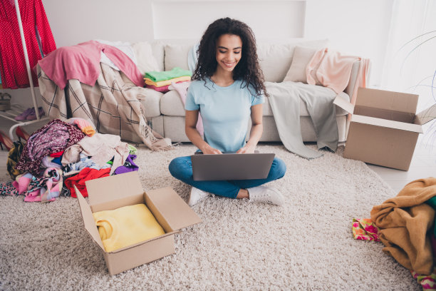 漂亮的年轻女孩的全尺寸照片使用笔记本电脑网上购物堆叠衣服公寓室内图片下载