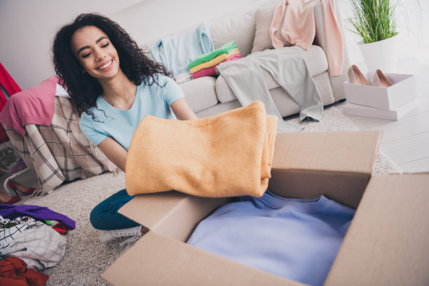漂亮年轻女孩的全尺寸照片，坐在地板上，拿着放衣服，东西盒子，公寓在室内图片下载