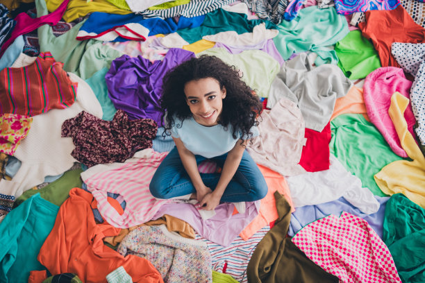 上图是漂亮的年轻女孩坐在室内凌乱的衣服上的全身照片图片下载