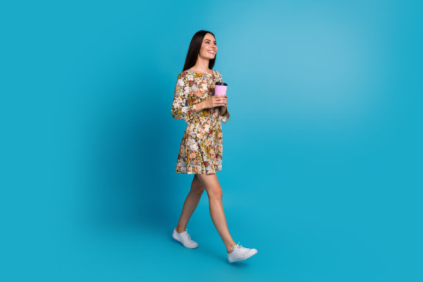 开朗漂亮的女士穿着印花衣服散步享受饮料空空间孤立的蓝色背景的全身照片图片下载