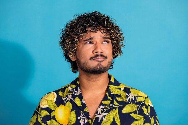 留着胡子、波浪发型、穿着印花衬衫的头脑男人的照片，在蓝色的背景上看命题的空白空间图片下载